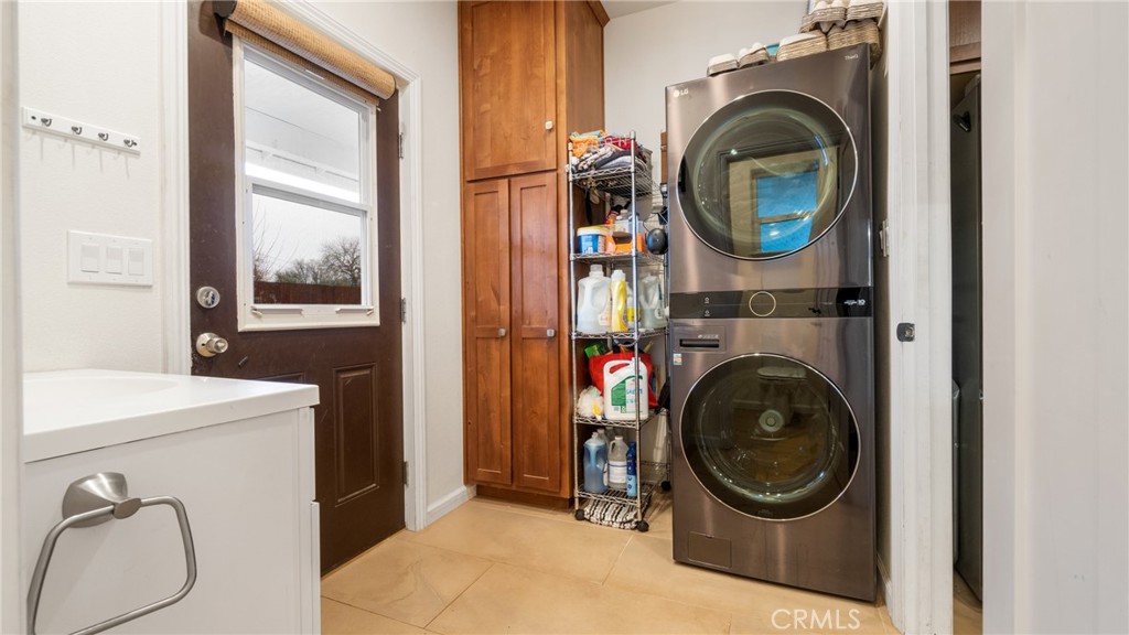 Laundry room with stacked washer and dryer beside tall wood cabinets and a utility sink.