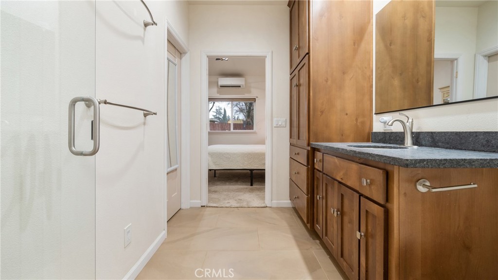 Bathroom vanity with wood cabinets and dark countertop, looking through a doorway into a bedroom.