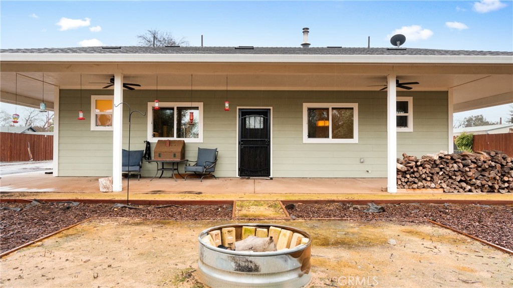Home’s covered backyard patio with outdoor seating, stacked firewood, and a circular fire pit.