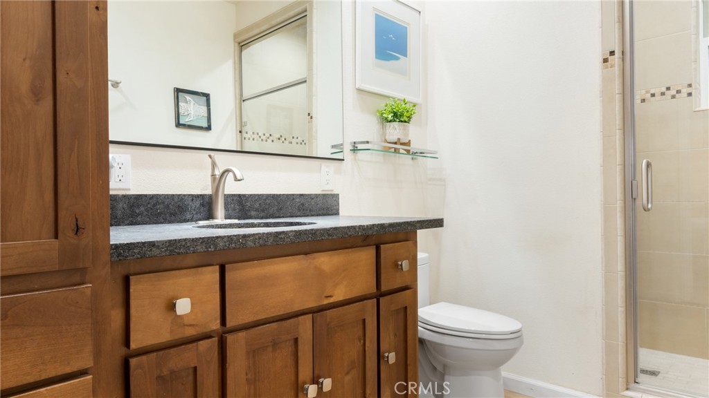 Bathroom with a wood vanity and dark countertop beside a toilet and glass-enclosed shower.