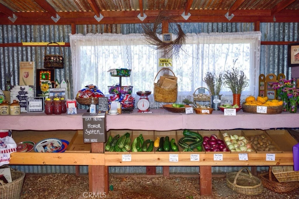 Covered farm stand displaying vegetables, fruit, jars, and packaged goods beneath a timber roof.