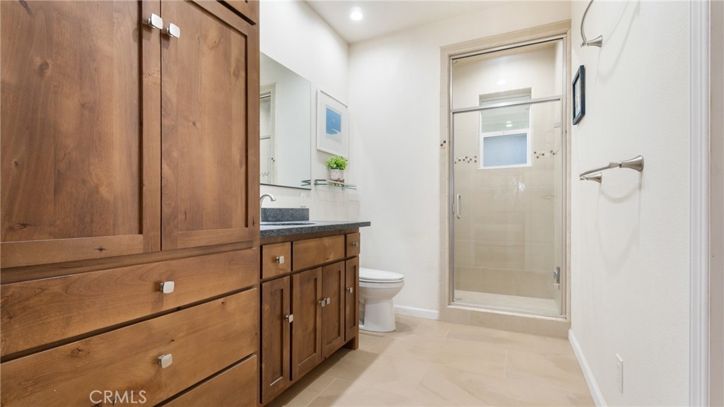 Bathroom with a large wood vanity, gray countertop, and glass-enclosed tiled shower.