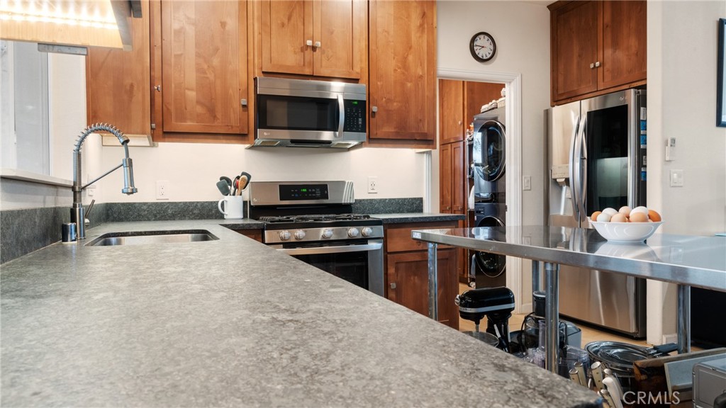 Kitchen with warm wood cabinets, gray stone counters, stainless appliances, and a stacked washer and dryer.