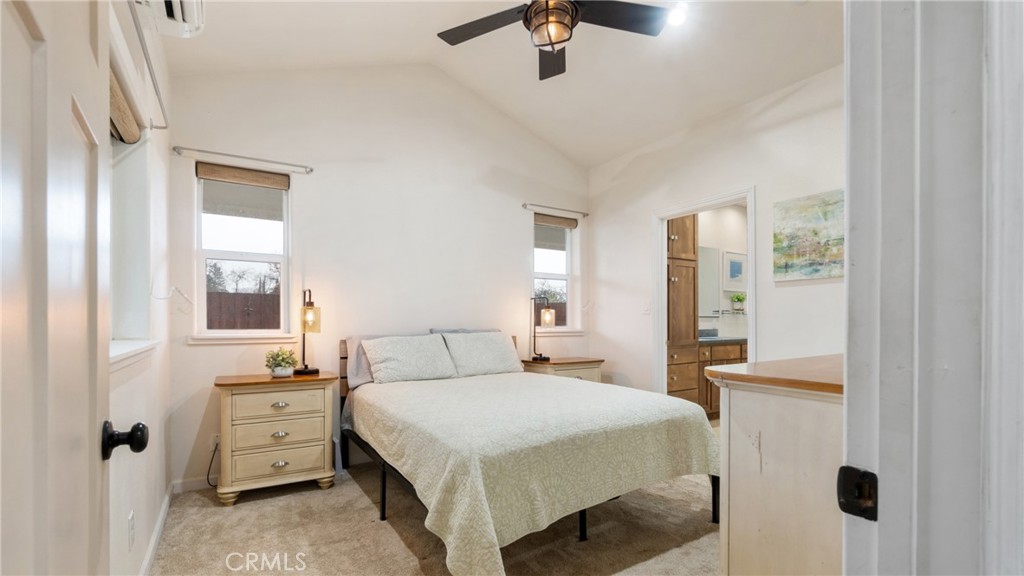 Bedroom with a light-colored bed between two windows and a ceiling fan.
