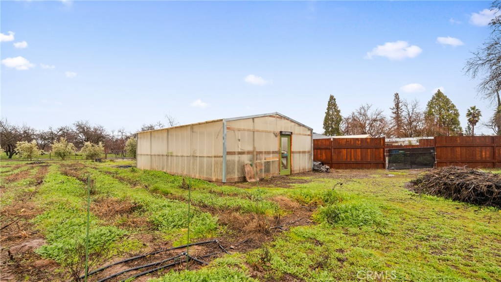 Greenhouse in a fenced backyard with garden beds and green groundcover.