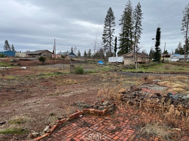 Vacant residential lot with brick patio remnants, nearby homes, and tall trees.