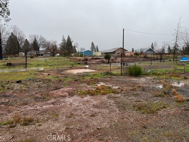 Vacant lot with muddy ground, sparse grass, wire fencing, and outbuildings in the distance.