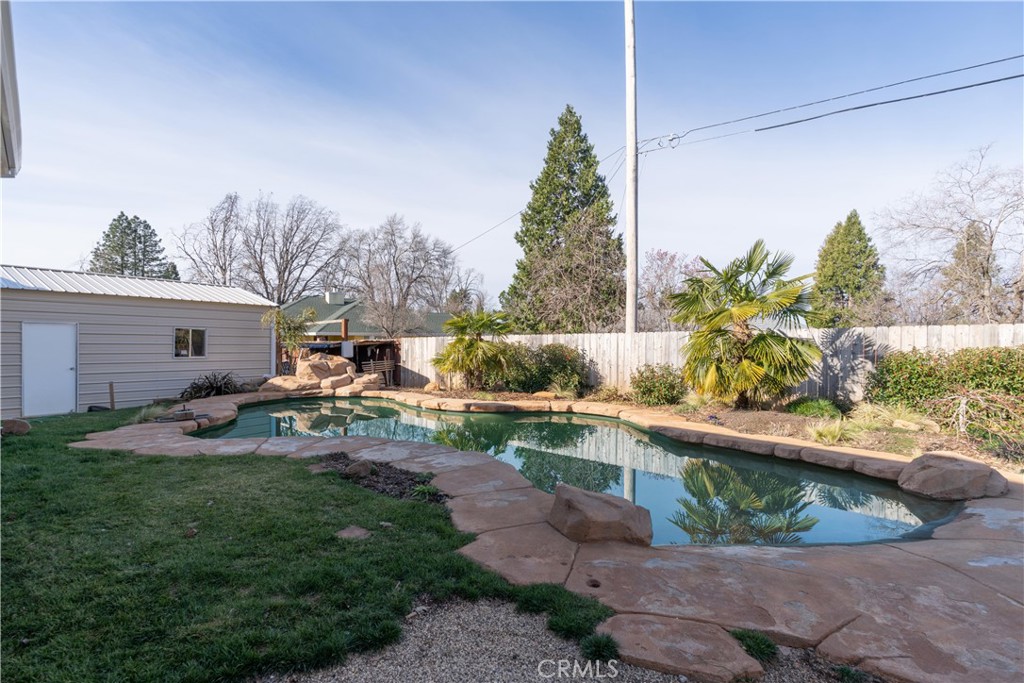 Backyard swimming pool edged with stone, beside a lawn and fenced garden.