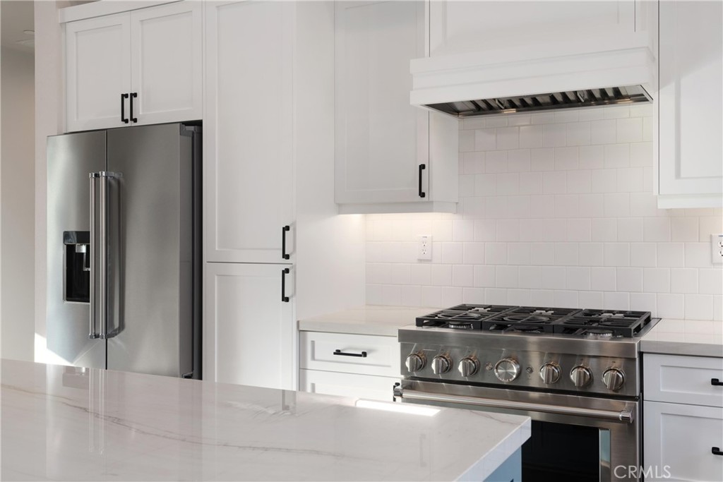 Kitchen with white shaker cabinets, stainless steel appliances, a gas range, and a veined stone island.