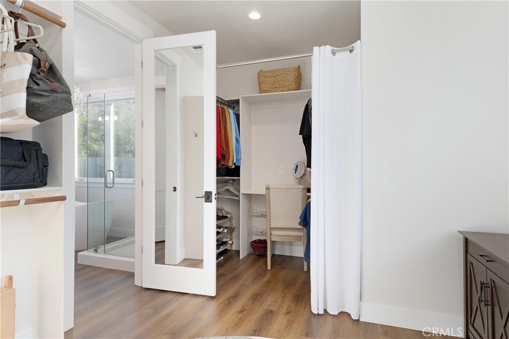 Walk-in closet with hanging clothes, shoe shelves, and an open door to a glass shower.