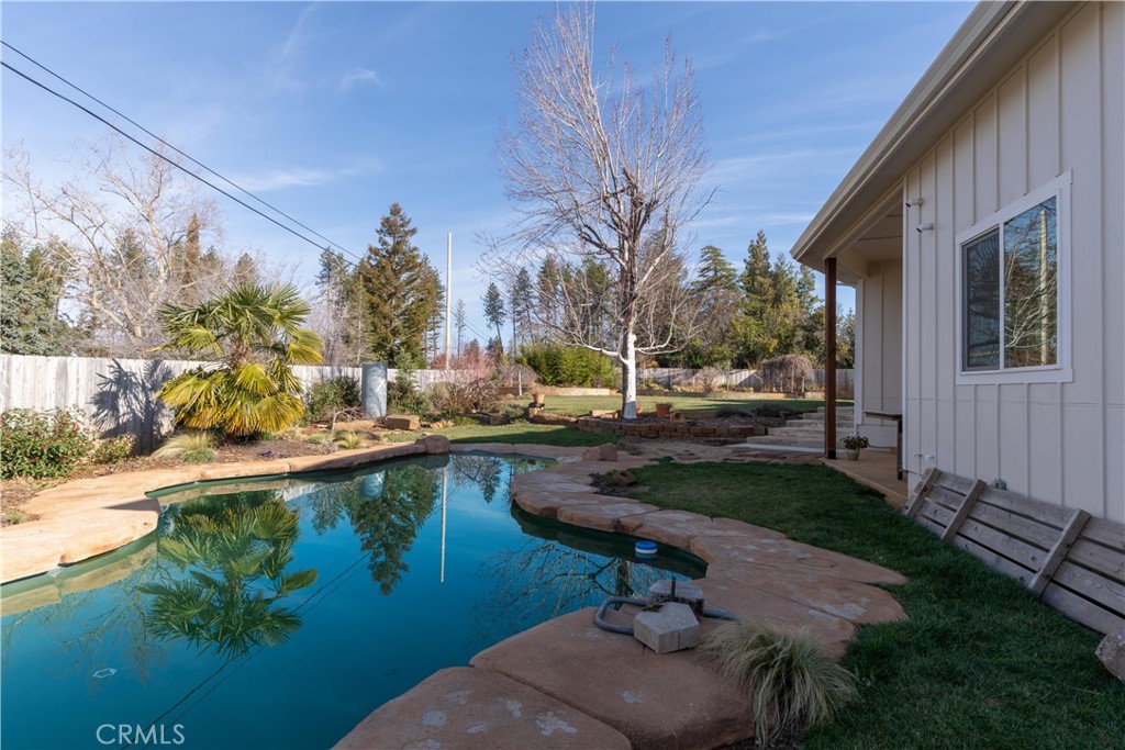 Backyard swimming pool with stone coping beside a fenced yard and the home's exterior.