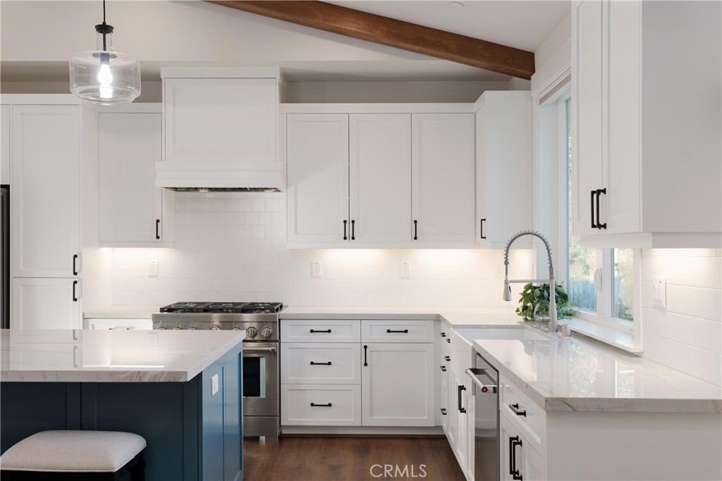 Bright kitchen with white cabinetry, a dark blue island, stainless steel range, and exposed wood ceiling beam.