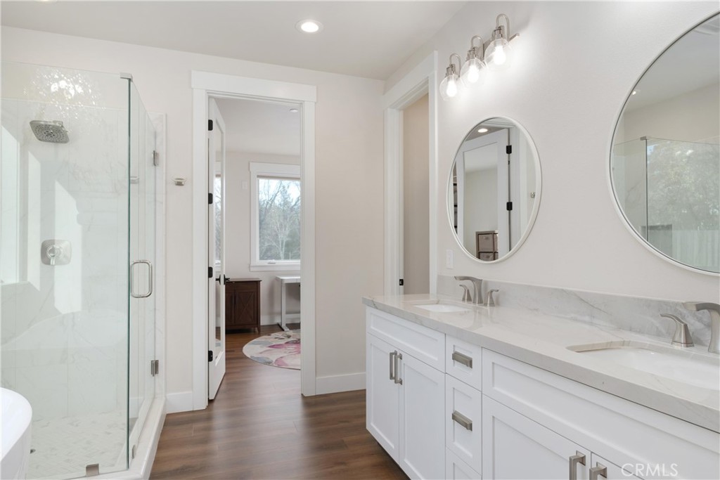 Bathroom with a long double vanity, round mirrors, and a glass-enclosed shower.
