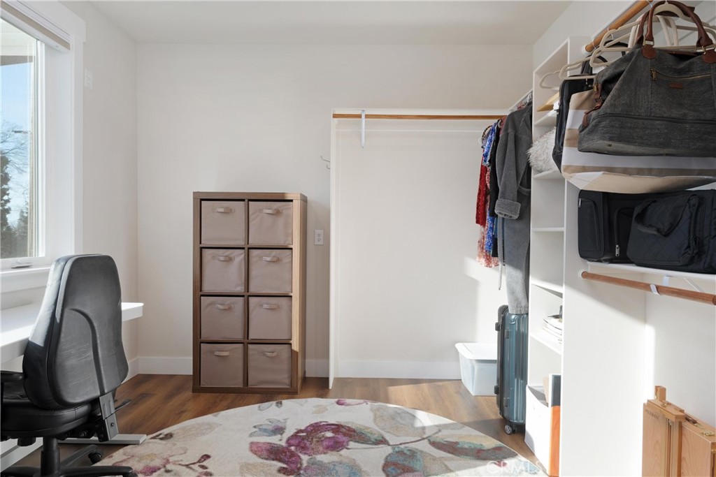 Walk-in closet with open clothing shelves, a desk, and a floral rug.
