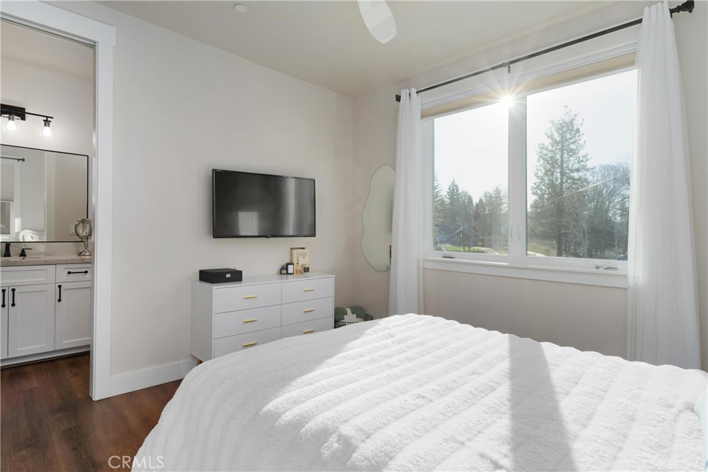 Bright bedroom with a white bed and large window overlooking trees; ensuite bathroom visible through the doorway.
