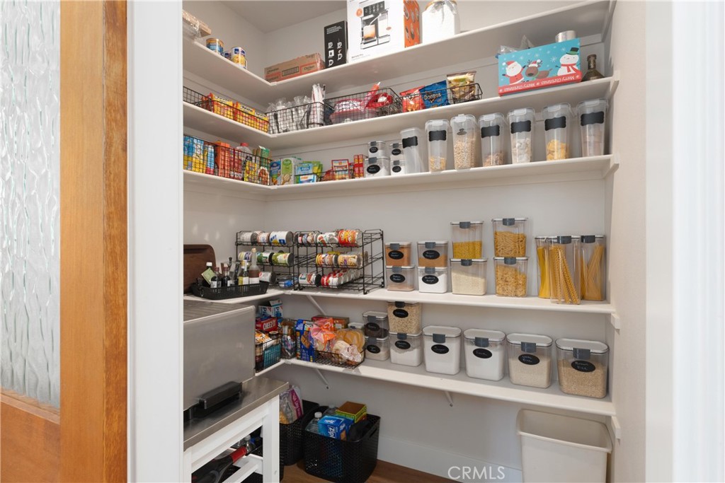 Walk-in pantry with white shelving, clear storage containers, baskets, and neatly arranged groceries.