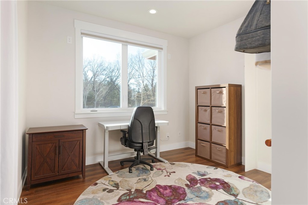 Furnished home office with a white desk beneath a large window and a floral rug.
