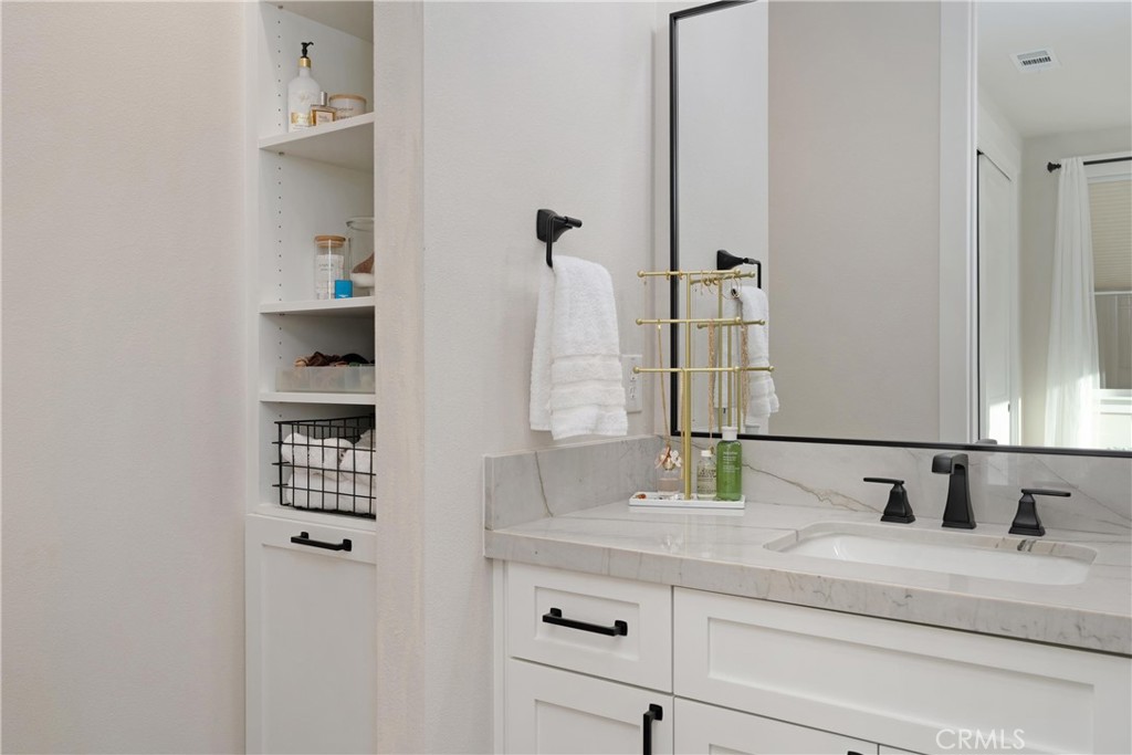Bathroom vanity with marble countertop, black fixtures, and built-in open shelving.