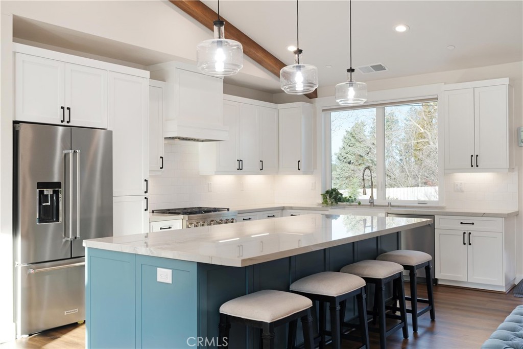 Modern kitchen with a blue island, white cabinetry, stainless appliances, and four bar stools.