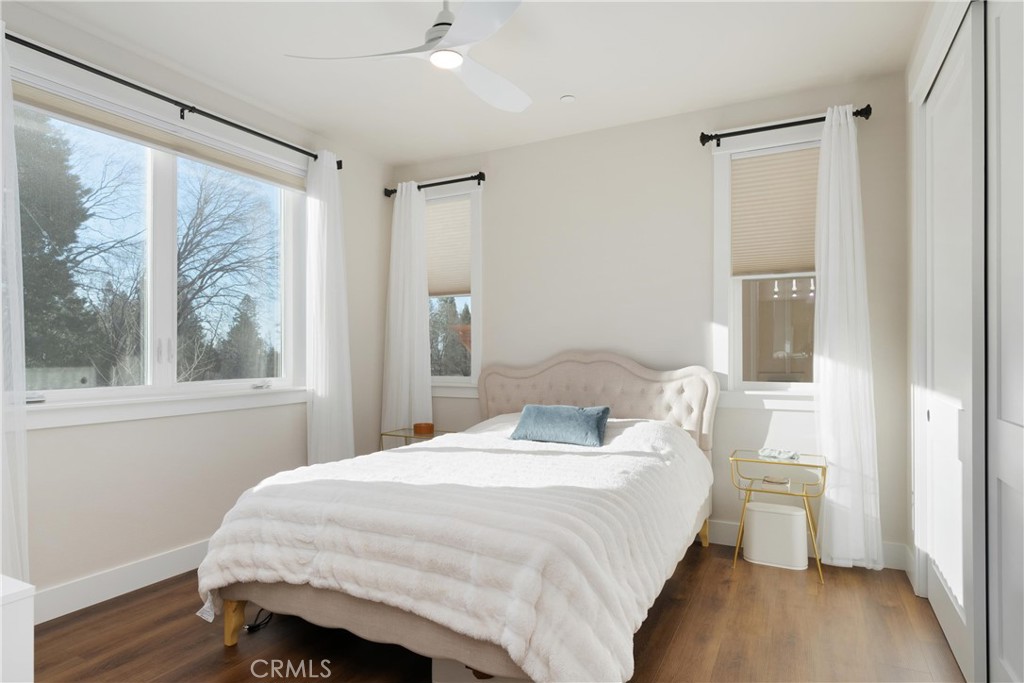 Bright bedroom with a white quilted bed, upholstered headboard, and large windows.