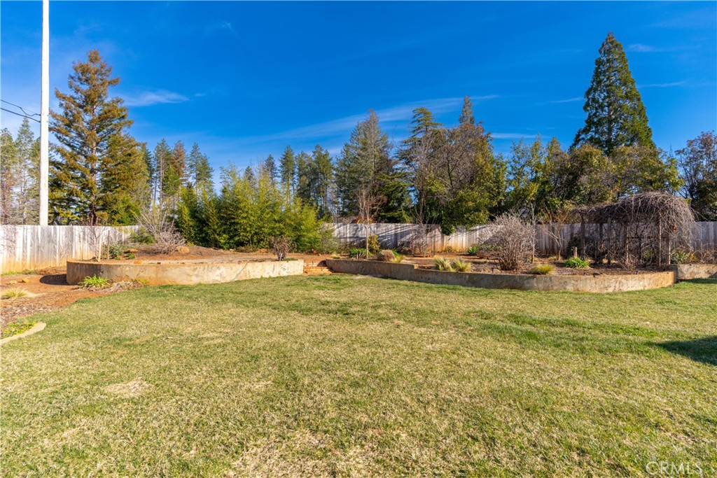 Backyard lawn bordered by raised planting beds, a wooden fence, and mature trees.