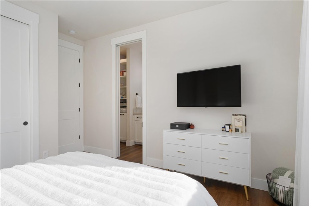 Bedroom with a white bed, wall-mounted television, and open doorway to a bathroom.