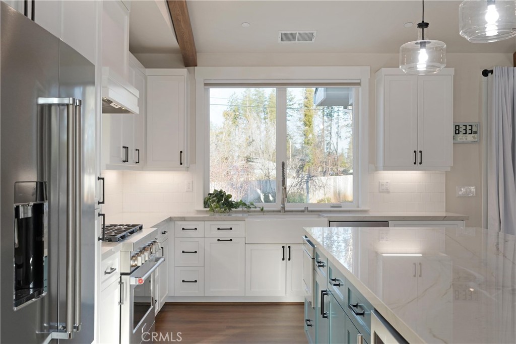 Modern white kitchen with a large island, stainless steel appliances, and a window overlooking trees.