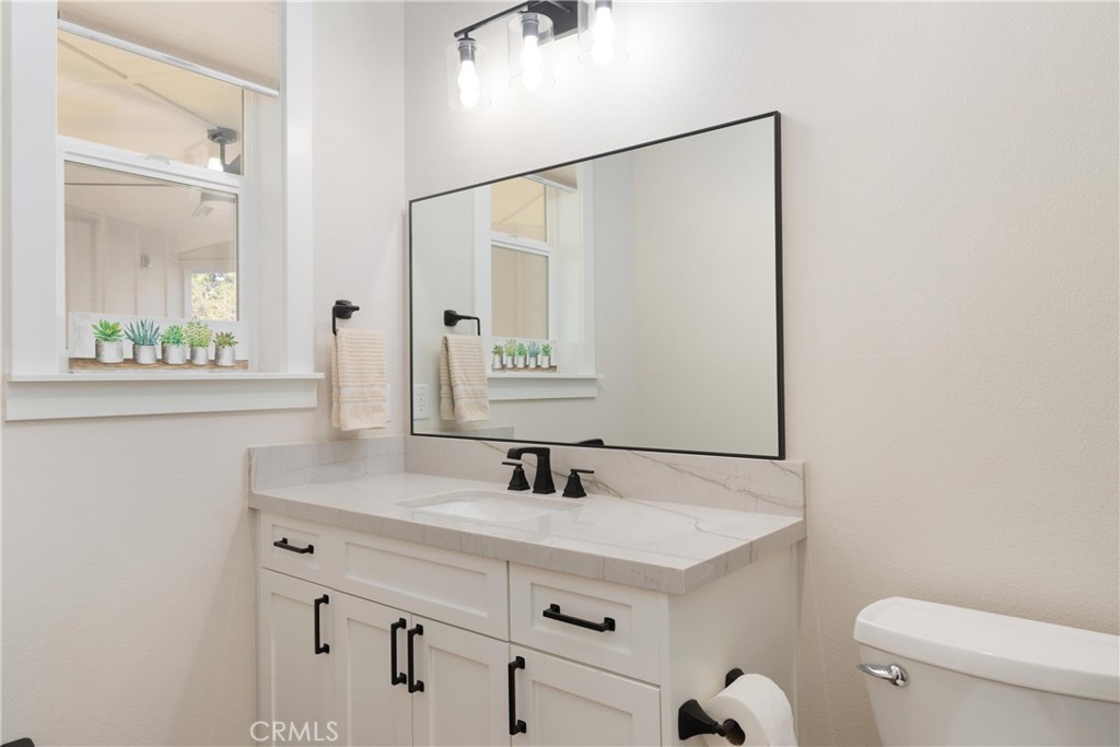 Bathroom vanity with a marble-look countertop, large mirror, and black fixtures beside a window.