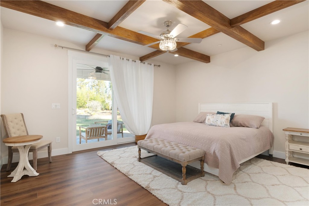 Bedroom with exposed wood ceiling beams, a large bed, and sliding glass doors opening to a patio.