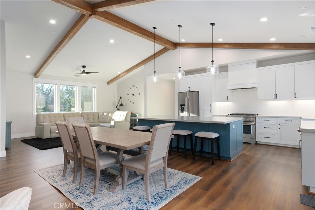 Open-plan kitchen and dining area with a blue island, vaulted ceilings, and exposed wood beams.