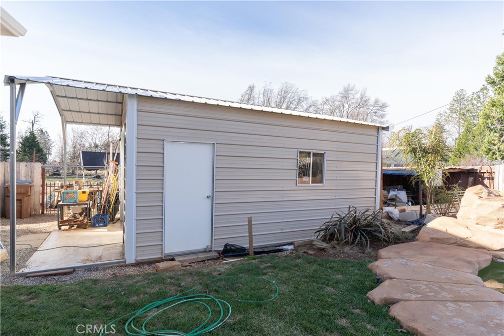 Metal-sided outbuilding with a white door, window, and attached covered work area.