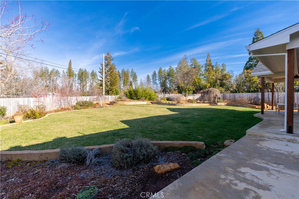 Backyard with a broad lawn, landscaped beds, mature trees, and a covered patio.