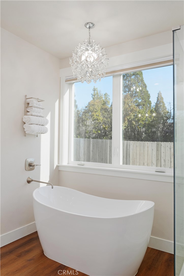 Bathroom with a freestanding tub, crystal chandelier, and large window overlooking trees.