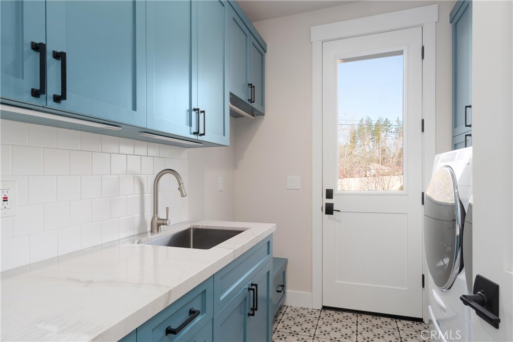 Laundry room with blue cabinets, a white sink counter, patterned tile floor, and front-loading washer and dryer.