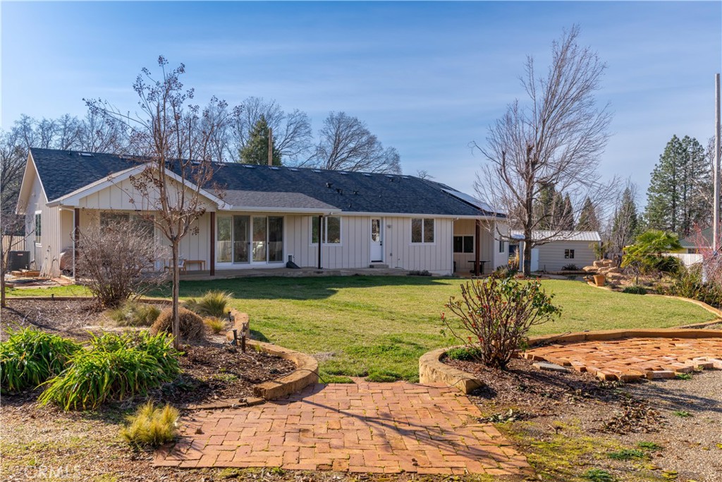 Single-story home behind a broad lawn, with a brick walkway and landscaped garden beds.
