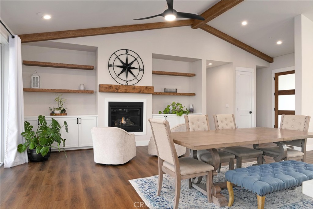 Open-plan living and dining room with a fireplace, built-in shelves, wood beams, and a long dining table.