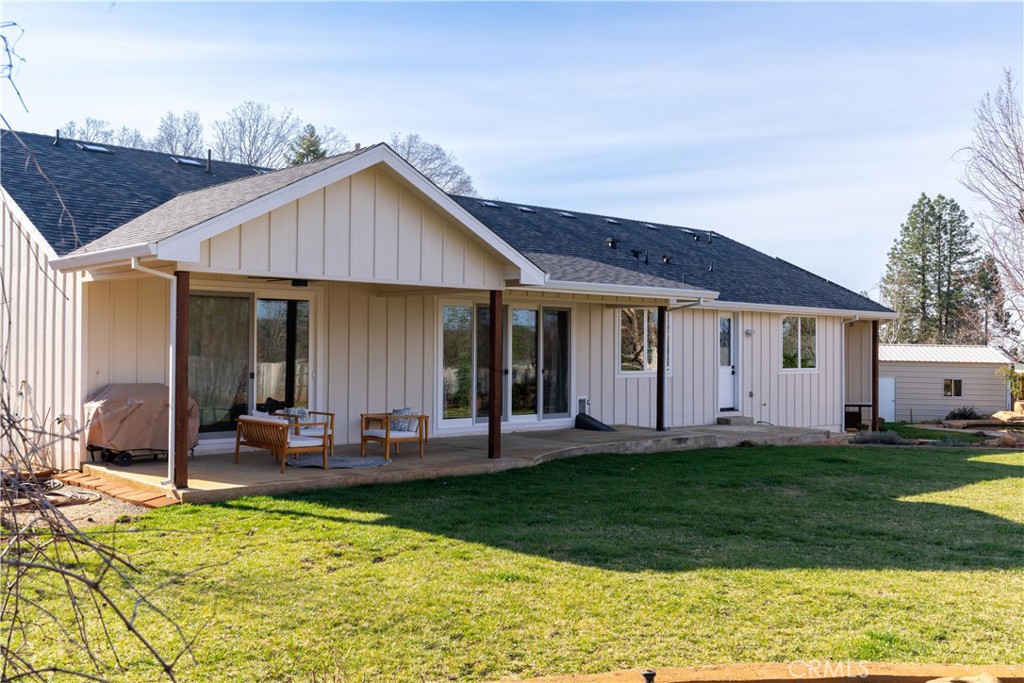 Rear of a light-colored home with a covered patio and outdoor seating beside a green lawn.