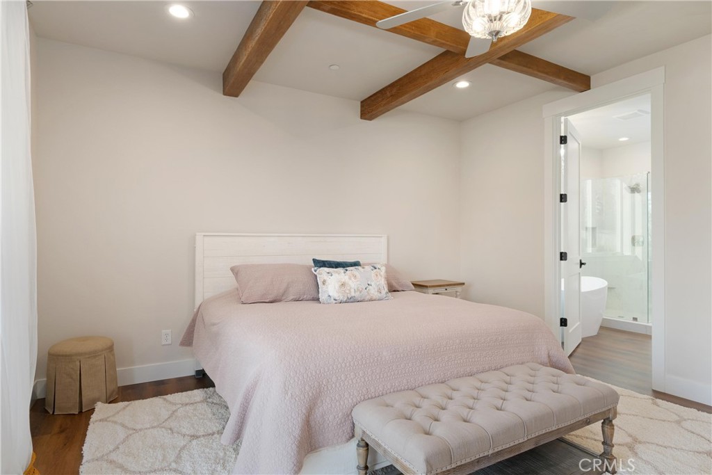 Bedroom with exposed wood ceiling beams, a pale pink bed, and an ensuite bathroom.