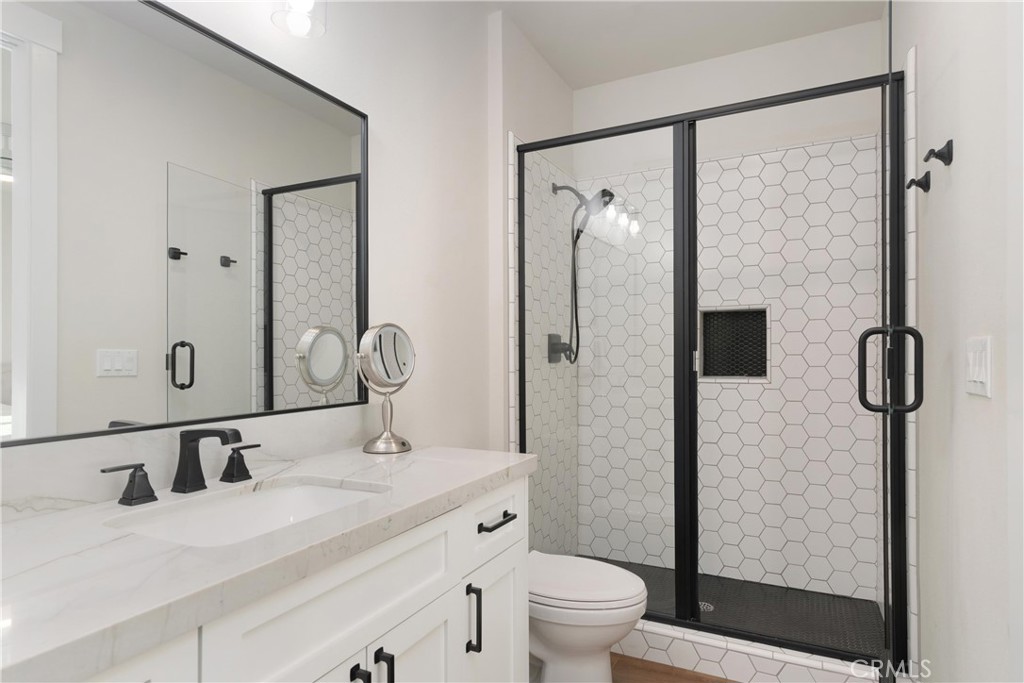 Modern bathroom with a white vanity and black-framed glass shower lined in hexagonal tile.