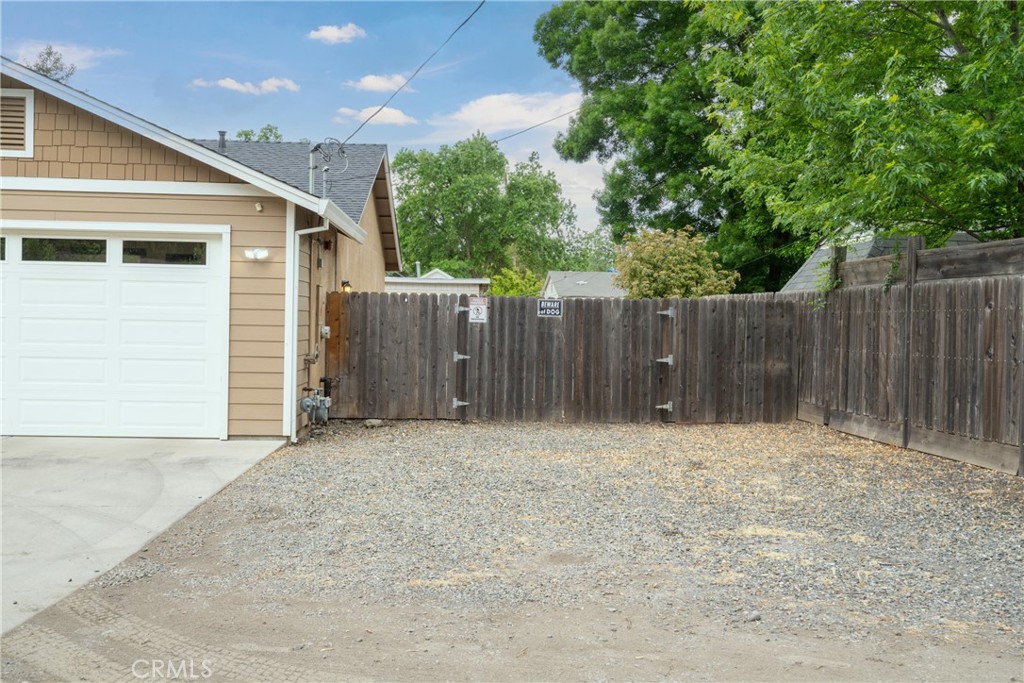 Detached garage beside a fenced gravel yard, with mature trees overhead.