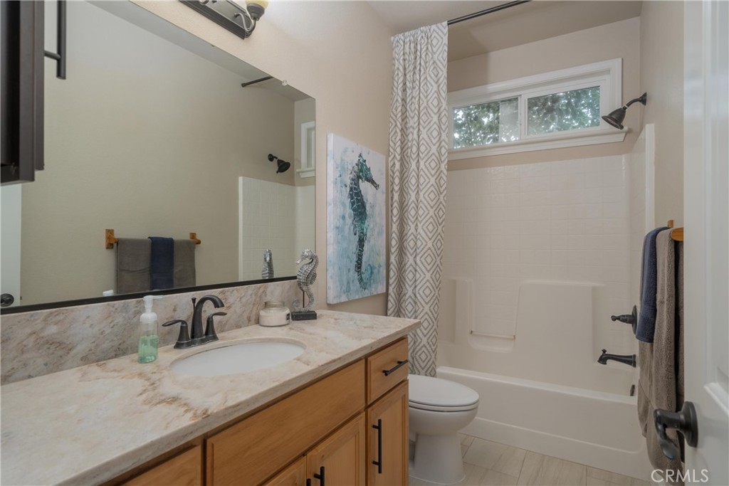 Bathroom with a wood vanity, large mirror, and bathtub beneath a high window.