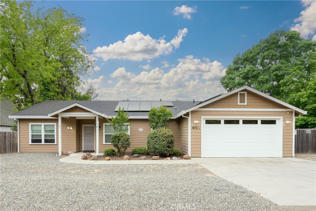 Single-story tan house with solar panels, a two-car garage, and a gravel front yard.