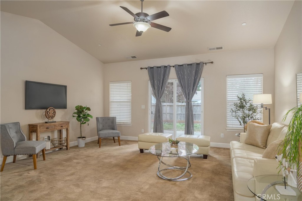 Living room with a vaulted ceiling, ceiling fan, and glass patio doors framed by gray curtains.