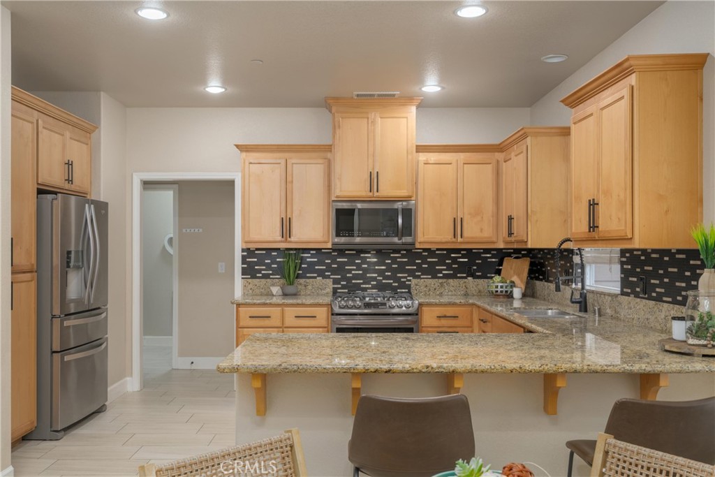 Kitchen with light wood cabinets, stainless steel appliances, granite counters, and a wide seating peninsula.