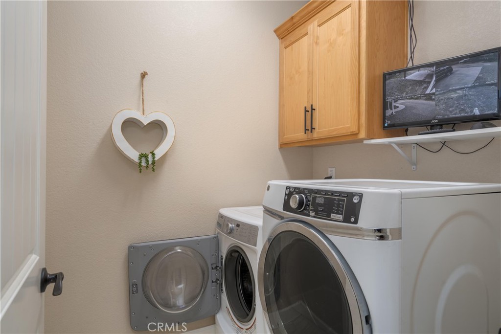 Laundry room with front-loading washer and dryer beneath wooden cabinets.