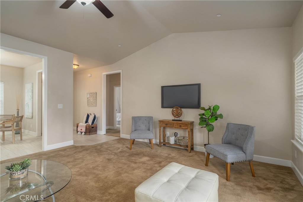 Staged living room with gray armchairs, a wall-mounted television, and an adjoining dining area.