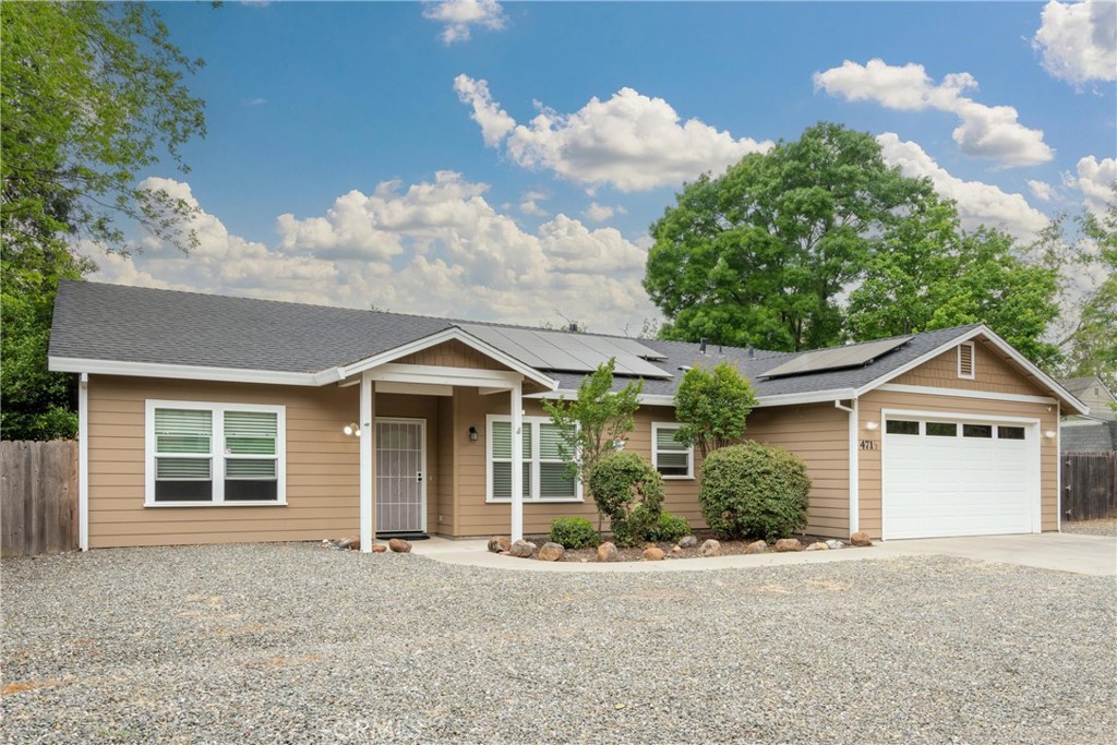 Single-story tan home with solar panels, attached garage, and broad gravel driveway.