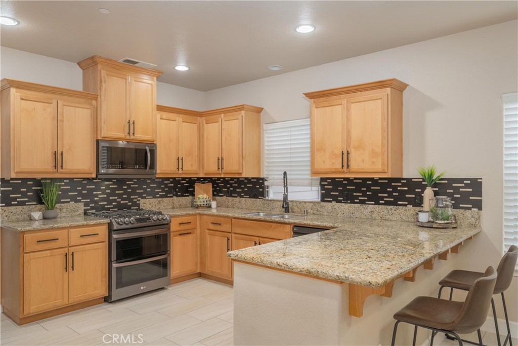 Kitchen with light wood cabinets, granite counters, a dark patterned backsplash, and a large peninsula.