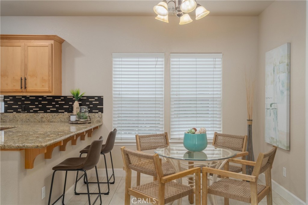 Dining area with a round glass-top table and woven chairs beside a granite kitchen peninsula.