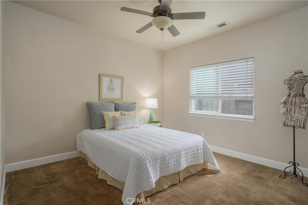 Staged bedroom with a white quilted bed, ceiling fan, and window with blinds.